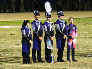 Five marching band members on the field with an award