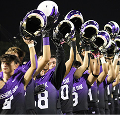 Football team lined up on field and raising their helmets in the air